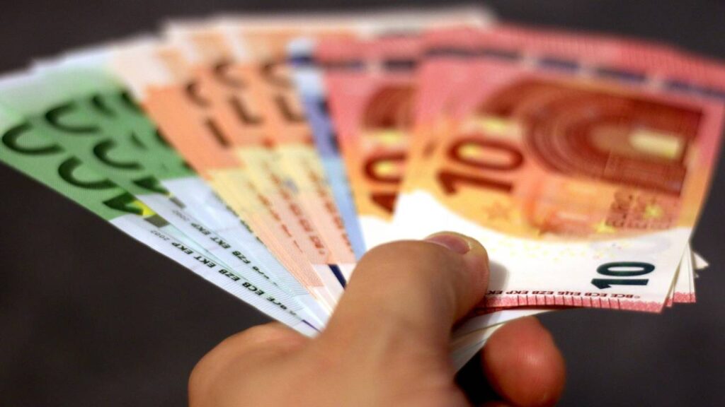 A close-up photo of a person holding a stack of Euro bills